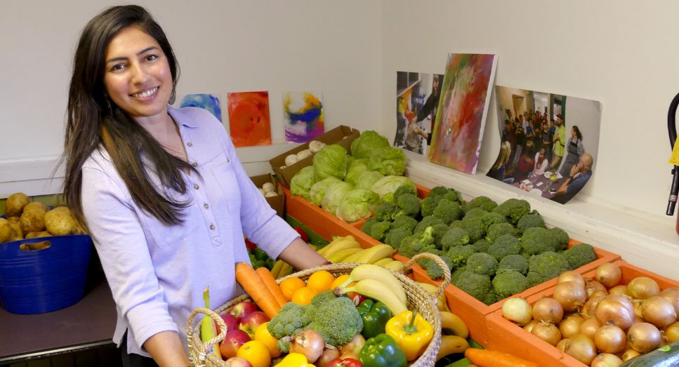 a smiling woman holding a big basket for fresh vegetables surrounded by vegetables